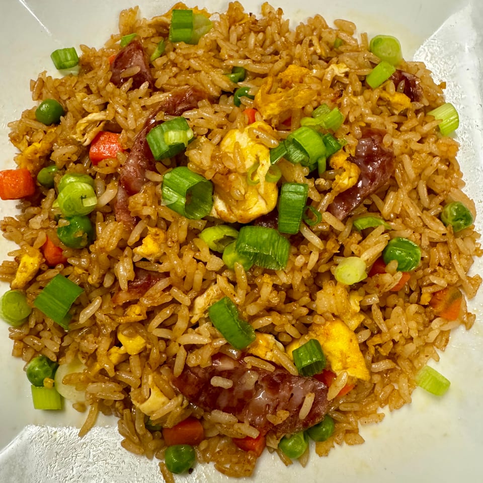 Fried rice with scrambled egg, Chinese sausage, peas, carrots, and chopped green onions on a white plate.
