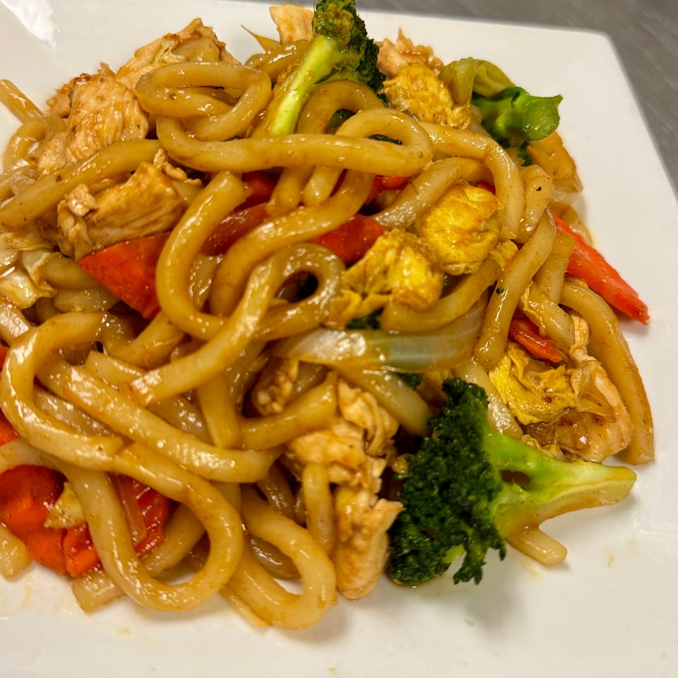 Stir-fried thick noodles with chicken, broccoli, cabbage, onions, and red bell peppers on a white plate.