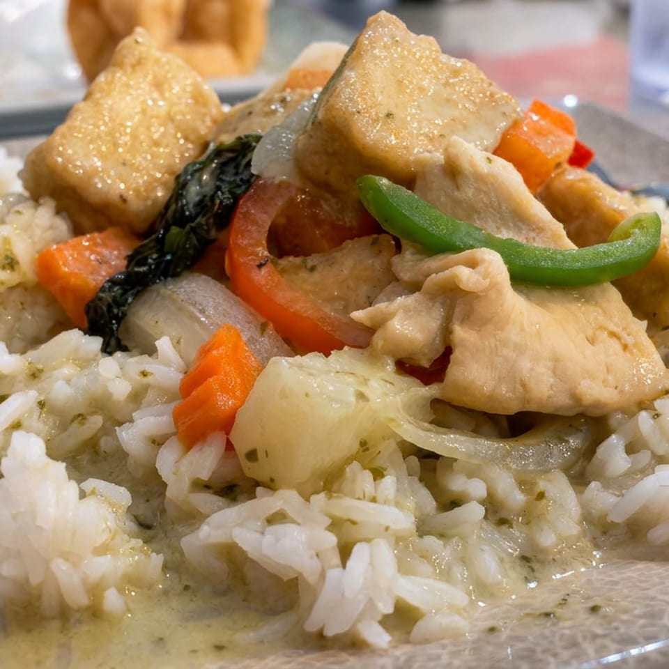 Plate of white rice topped with creamy chicken, carrots, onions, green pepper, and dark leafy vegetables.