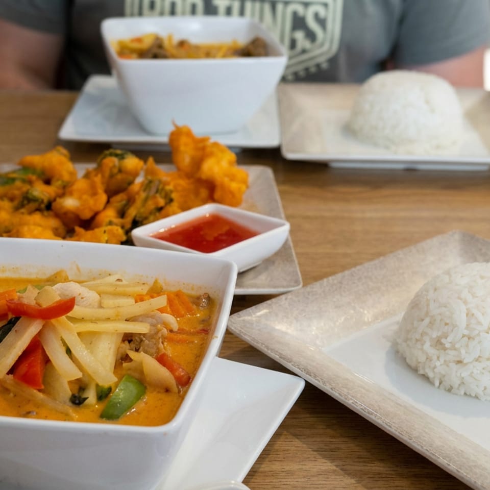 Thai curry with vegetables, jasmine rice, fried appetizers, and dipping sauce served on a wooden restaurant table.